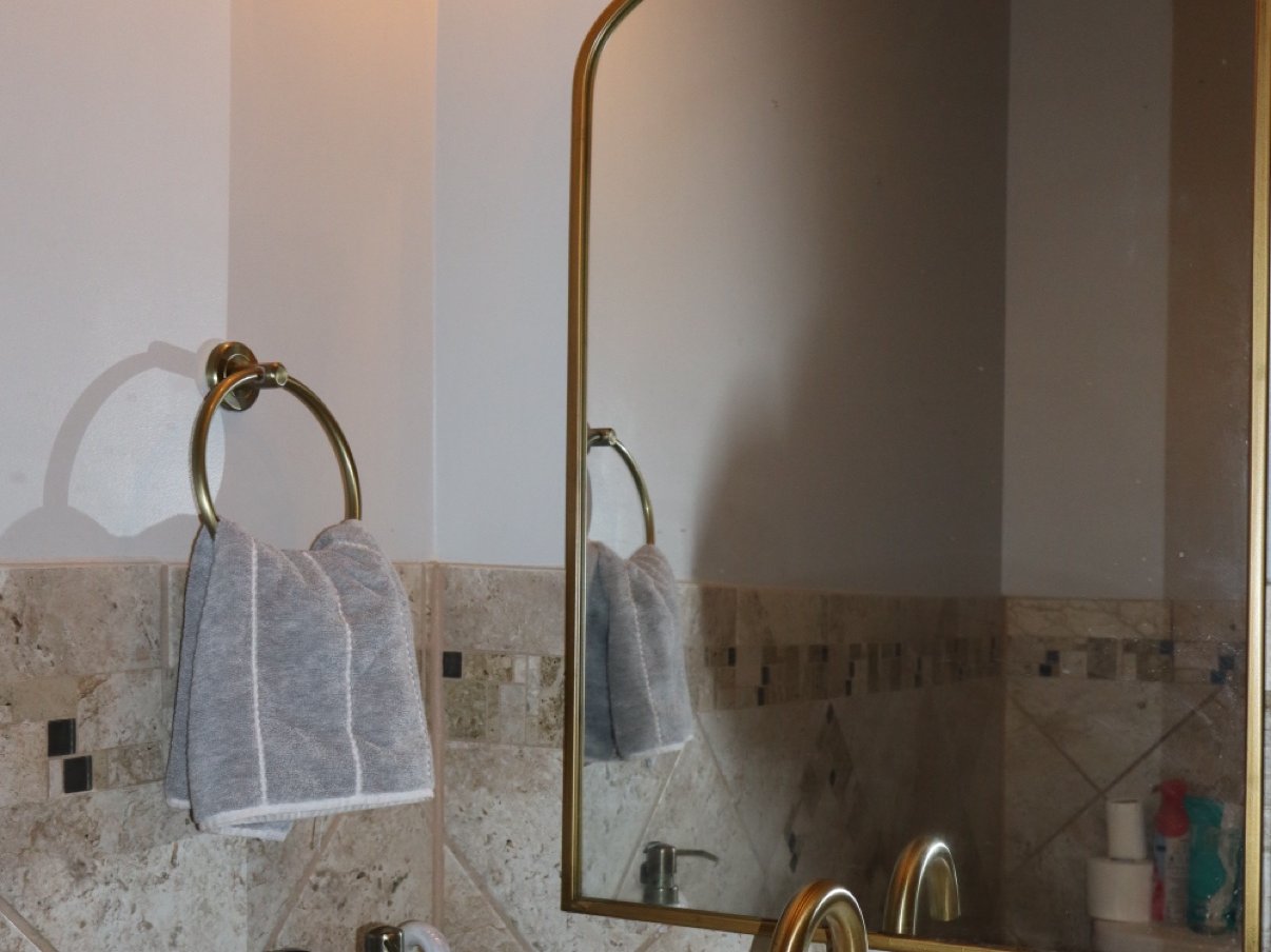 Travertine tile bathroom with a gold-framed mirror and brushed gold fixtures, remodeled by Carolina Construction Bros