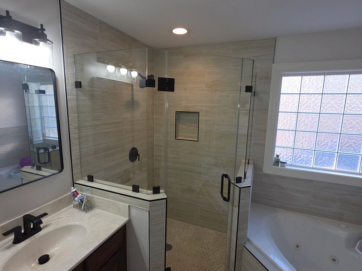 Remodeled bathroom with a corner glass shower, hex tile floor, matte black fixtures, and a soaking tub, by Carolina Construction Bros of Fuquay-Varina, NC