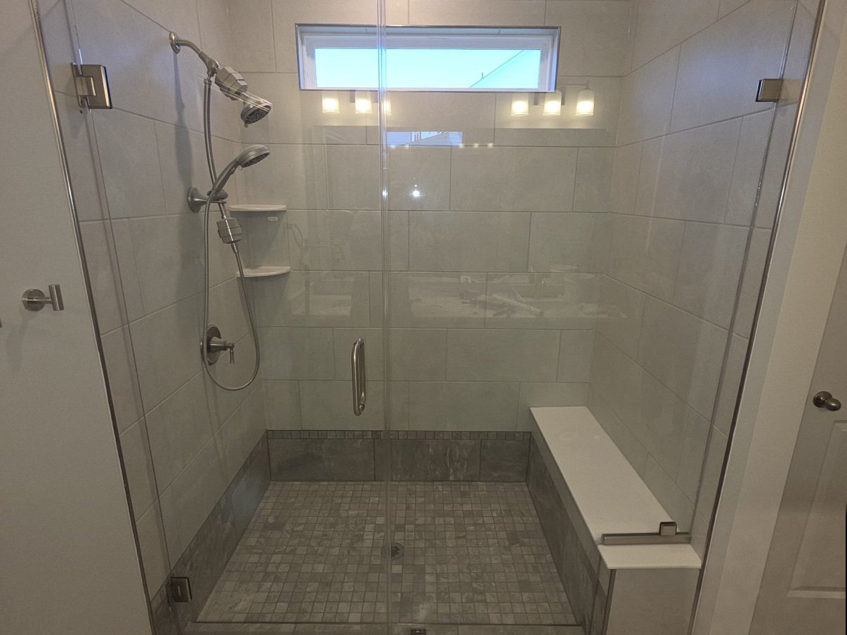 Large tile shower with a frameless glass enclosure, bench seat, transom window, and brushed nickel fixtures